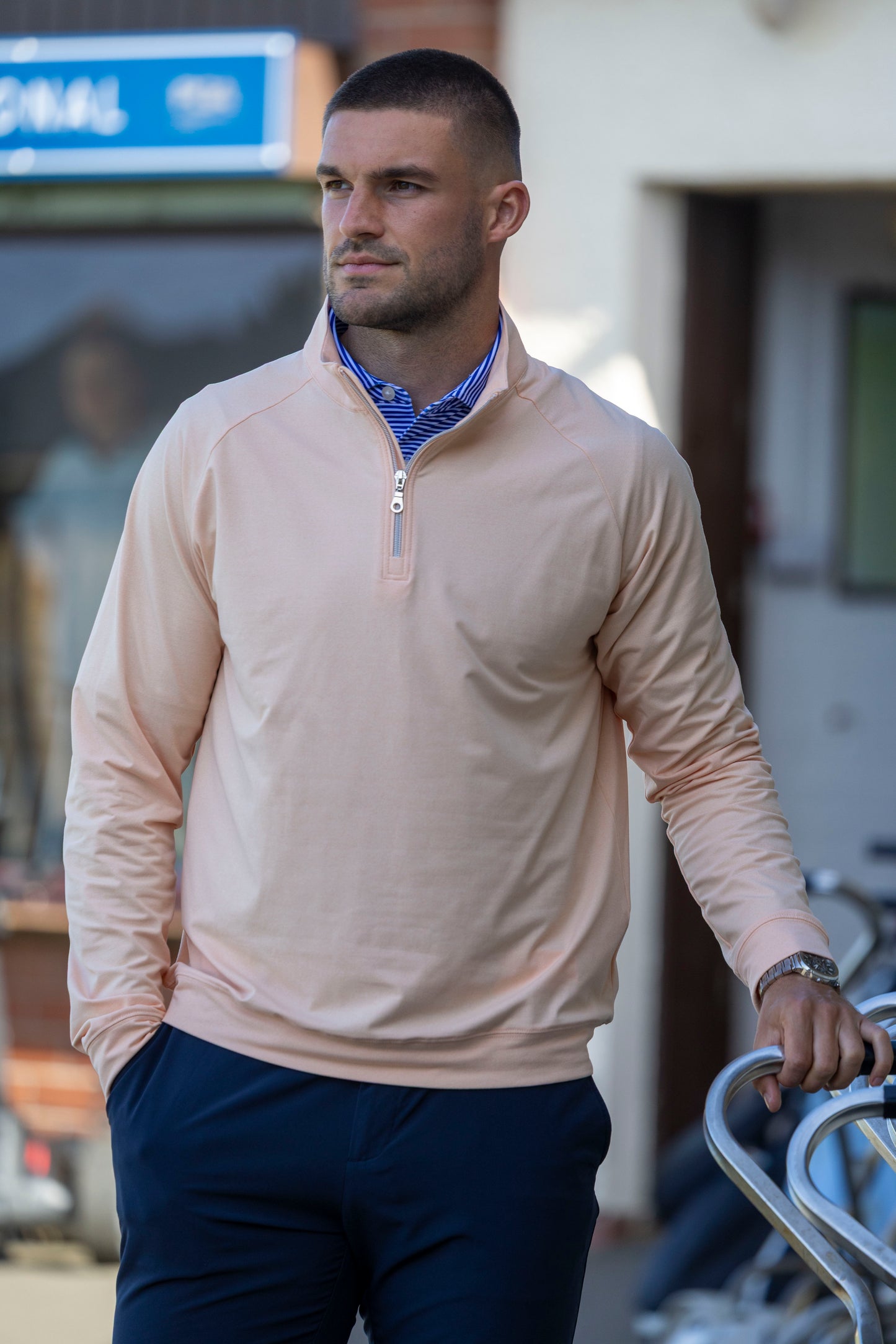 Innes Cameron wearing a beige long-sleeve shirt with a zipper and blue pants, standing outdoors.